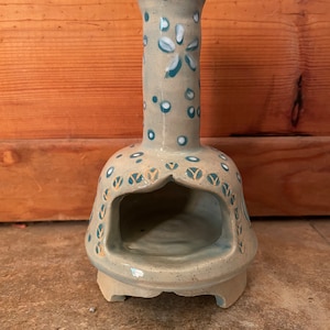 Può includere: Un piccolo camino in ceramica grigia con un design floreale bianco e blu. Il camino ha una piccola apertura nella parte anteriore e una base arrotondata.