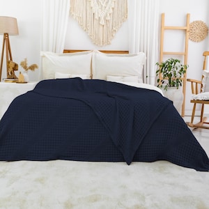 May include: A dark navy blue blanket with a textured waffle weave pattern draped over a bed. The blanket features a uniform grid-like structure across its entire surface, providing a consistent tactile appearance and a deep, solid color finish.