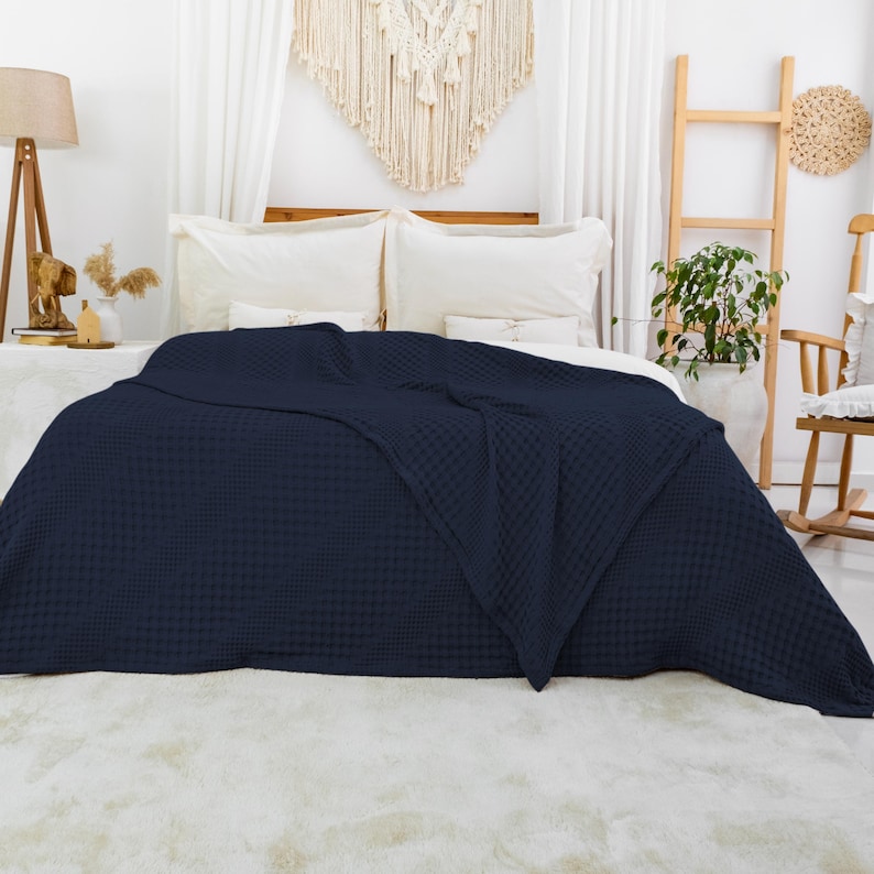 May include: A dark navy blue blanket with a textured waffle weave pattern draped over a bed. The blanket features a uniform grid-like structure across its entire surface, providing a consistent tactile appearance and a deep, solid color finish.