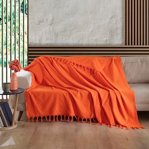 May include: A bright orange throw blanket with fringe trim draped over a white sofa. The blanket is made of a soft, textured fabric.
