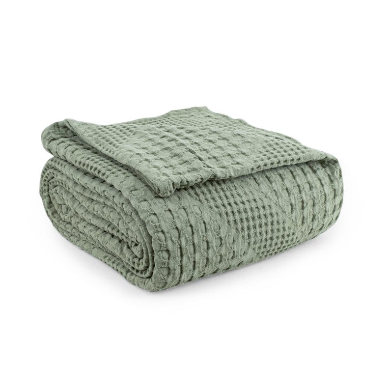 May include: A sage green blanket featuring a distinct waffle weave texture. The fabric is folded into a neat, rectangular stack, showcasing the uniform grid pattern across the entire surface of the textile. The material has a soft, matte appearance.