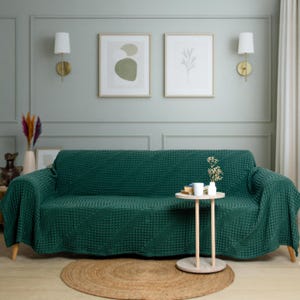 May include: A dark green sofa cover with a textured waffle-knit pattern draped over a couch. The cover features a consistent grid-like design across the entire surface, providing a uniform appearance that fits snugly over the furniture frame.