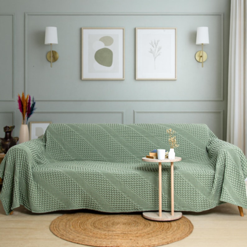 May include: A sage green sofa cover featuring a textured, diagonal knit pattern that drapes over the entire couch. The fabric has a consistent, raised geometric weave throughout, providing full coverage for the seat, backrest, and armrests.