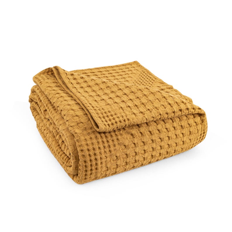 May include: A folded mustard yellow blanket featuring a distinct waffle weave texture. The fabric has a grid-like pattern across the entire surface, with a smooth, finished edge visible along the top fold of the textile product.