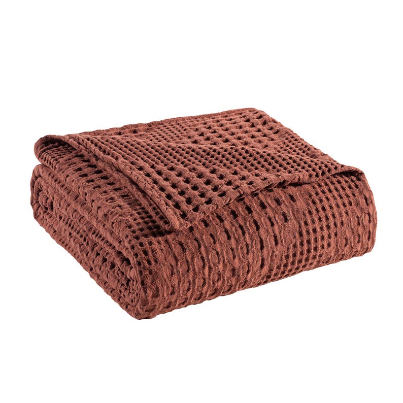 May include: A folded blanket in a deep terracotta red color featuring a prominent waffle weave texture. The fabric has a grid-like pattern created by the raised square sections of the weave, giving the textile a thick and dimensional appearance.