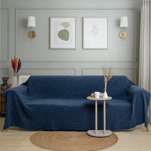 May include: A deep navy blue sofa cover with a textured, raised waffle-knit pattern draped over a couch. The fabric features a consistent grid-like design across the entire surface, providing a uniform appearance that covers the back and seat.