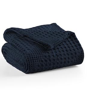May include: A folded navy blue waffle-weave blanket. The blanket is made of a soft material and has a textured, grid-like pattern. The blanket is folded over itself, with the top portion draped over the bottom.