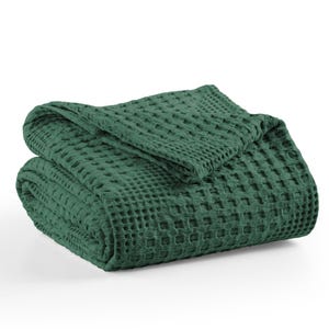 May include: A dark forest green blanket featuring a prominent waffle weave texture. The fabric is folded into a neat, layered stack, showcasing the square grid pattern across the entire surface of the textile. The edges are finished with a hem.
