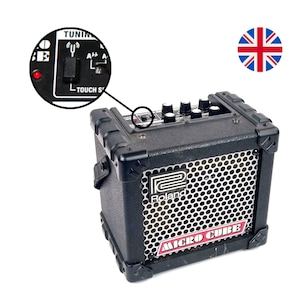 May include: A black Roland Micro Cube guitar amplifier with a silver speaker grille and red lettering. The amplifier has a tuner, a headphone jack, and a touch sensitive switch.