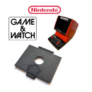 Könnte beinhalten: Eine rote und schwarze Nintendo Game & Watch Handheld-Spielkonsole mit dem Text "Mario's Cement Factory" auf dem Bildschirm. Die Konsole steht auf einem schwarzen, rechteckigen, 3D-gedruckten Ständer mit einem Loch in der Mitte und einem Haussymbol auf der Vorderseite.
