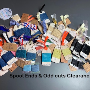 May include: A collection of assorted thread spools and yarn remnants wrapped around small cardboard tags. The threads come in various colors including blue, black, green, and beige, with some featuring attached ribbons and handwritten labels.