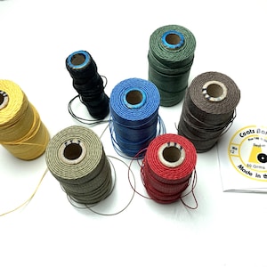 May include: A collection of seven spools of Coats Barbour linen thread in yellow, black, light green, blue, dark green, red, and brown. Each spool is labeled 50 Grms and Made in the EU. The thread is wound on cardboard cores with blue centers.