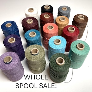May include: A collection of eighteen cylindrical spools of thread in various colors including white, black, grey, brown, red, blue, green, and purple. The spools are arranged in a group with the text WHOLE SPOOL SALE! printed at the bottom.