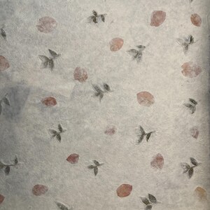 May include: A sheet of handmade paper with a delicate pattern of pressed leaves and flowers. The paper is a light beige color with a subtle texture. The leaves and flowers are a light brown and pink color.