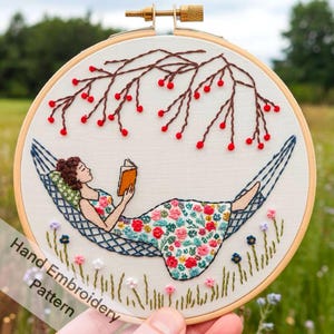 Könnte beinhalten: Handgesticktes Stickrahmen-Kunstwerk, das eine Person zeigt, die in einer Hängematte liest. Die Person trägt ein Blumenkleid. Das Design umfasst einen Ast mit roten Beeren und kleinen Blumen. Der Text "Hand Embroidery Pattern" ist sichtbar.