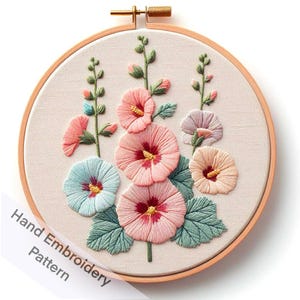 May include: A hand-embroidered hoop art piece featuring pink, blue, and white flowers with green leaves on a beige fabric background. The hoop is made of wood and has a gold finish.