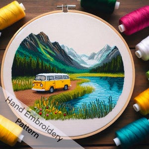 May include: Hand embroidery pattern of a yellow vintage van driving through a mountain landscape with a lake. The pattern includes mountains, trees, grass, and a lake.