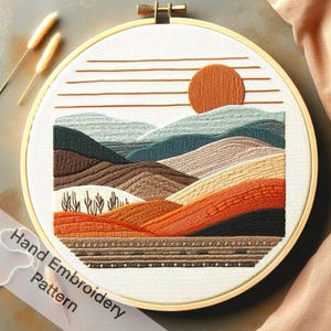 May include: Hand embroidery pattern featuring a sunset over a landscape of mountains in shades of brown, orange, and teal. The pattern is stitched on white fabric in a round embroidery hoop.
