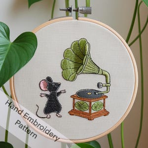 May include: Hand embroidery pattern featuring a black mouse listening to a vintage green gramophone with a black record. The gramophone is on a wooden base with green details. The pattern is on a beige fabric background.