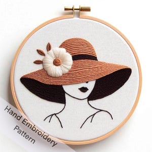 Op de afbeelding: Handborduurpatroon met een vrouw die een brede hoed met een bloem draagt. De hoed is bruin en de bloem is wit. Het gezicht van de vrouw is omlijnd met zwarte draad.