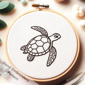 Puede incluir: Un diseño de tortuga marina bordado a mano en blanco y negro sobre una tela blanca estirada en un aro de bordado de madera. El texto "Hand Embroidery Pattern" es visible en la esquina inferior izquierda de la imagen.