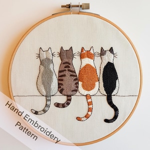 Puede incluir: Patrón de bordado a mano con cuatro gatos sentados en fila, mirando hacia arriba. Los gatos son grises, atigrado marrón, atigrado naranja y blanco y negro. El patrón está en una tela blanca en un aro de bordado de madera.