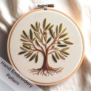 May include: A hand-embroidered olive tree pattern in a wooden embroidery hoop. The tree is depicted with green and brown thread, and the roots are brown.