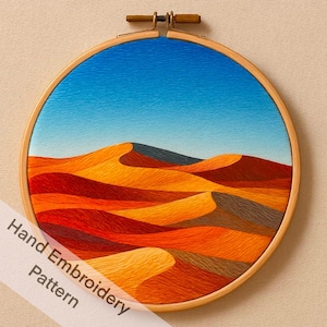 Puede incluir: Bordado a mano que representa un paisaje desértico con dunas de arena en tonos naranja, rojo y amarillo bajo un cielo azul. La obra está enmarcada en un aro de madera redondo. El texto "Hand Embroidery Pattern" es visible.