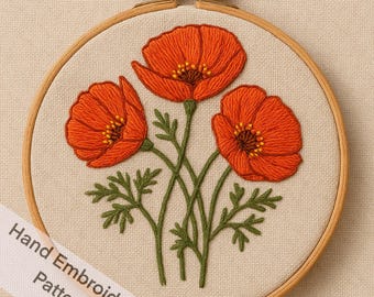 May include: Hand-embroidered poppy flowers in a wooden embroidery hoop. The poppies are a vibrant orange with yellow centers, green stems, and leaves. The text "Hand Embroidery Pattern" is on a white ribbon.