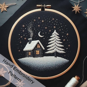 Könnte beinhalten: Stickbild mit Stickerei, das eine schneebedeckte Hütte mit einem beleuchteten Fenster, einen Kiefernbaum und einen Halbmond in einem sternenklaren Nachthimmel zeigt. Der Stickrahmen ist aus Holz mit einem schwarzen Stoffhintergrund.