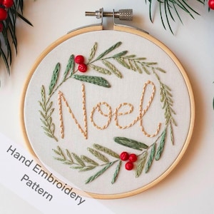 May include: A hand embroidery pattern featuring a wreath of green leaves and red berries with the word "Noel" stitched in the centre. The pattern is displayed in a wooden embroidery hoop.