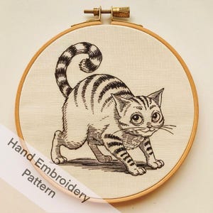 May include: Black and white hand embroidery pattern of a cat with a curled tail, in a wooden embroidery hoop.