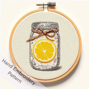 May include: A hand embroidery pattern featuring a mason jar with a lemon slice inside. The jar is tied with a brown ribbon and has a black outline. The lemon slice is yellow with a white center.
