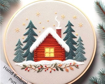 May include: Embroidered hoop art featuring a red cabin with a snowy roof and a yellow window, surrounded by green trees and a snowy ground. The hoop is decorated with a garland of green leaves and red berries. The text "Hand Embroidery Pattern" is visible at the bottom of the hoop.