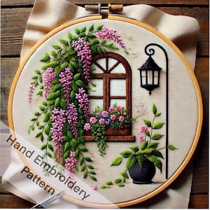 May include: Hand embroidery pattern featuring a window with a flower box, a lamppost, and a vine with pink flowers. The embroidery is framed in a wooden hoop.
