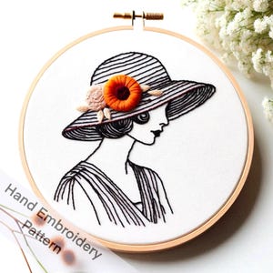 May include: Hand embroidery pattern of a woman wearing a wide-brimmed hat with a floral embellishment. The hat is striped and the woman's hair is styled in a bob. The embroidery is done in black thread on white fabric.