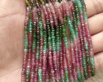 Pode incluir: Fios de contas de turmalina coloridas em tons de rosa, verde e castanho. As contas são pequenas, facetadas e estão enfiadas. As contas são seguradas em uma mão, mostrando as variações naturais de cor e textura.