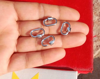 May include: A collection of five small, silver-colored oval carabiner clips. The clips are open and closed, showing their functionality. The background is a red surface with a partial view of a white box.