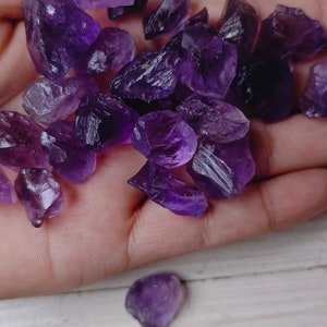 Pode incluir: Uma coleção de cristais de ametista brutos, em várias formas e tamanhos. Os cristais são de cor roxa escura e parecem recém-cortados. A imagem é tirada de perto, destacando a beleza natural das pedras preciosas.