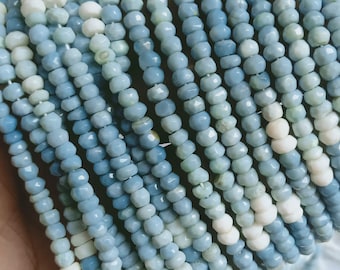 Puede incluir: Primer plano de múltiples hilos de cuentas facetadas en tonos azules y blancos. Las cuentas están ensartadas, creando una superficie texturizada. La paleta de colores varía del azul pálido a un tono más profundo, con cuentas blancas ocasionales.
