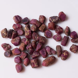 Puede incluir: Un conjunto de piedras preciosas de rubí en bruto, que muestran un tono rojo intenso con variaciones en forma y tamaño. Las piedras en bruto tienen un aspecto natural, sin pulir, con toques de marrón y dorado.