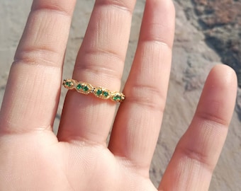 Puede incluir: Un anillo de oro con un patrón repetitivo de pequeñas piedras preciosas verdes de forma ovalada. El anillo está engastado con múltiples piedras de color esmeralda. El anillo está en un dedo.