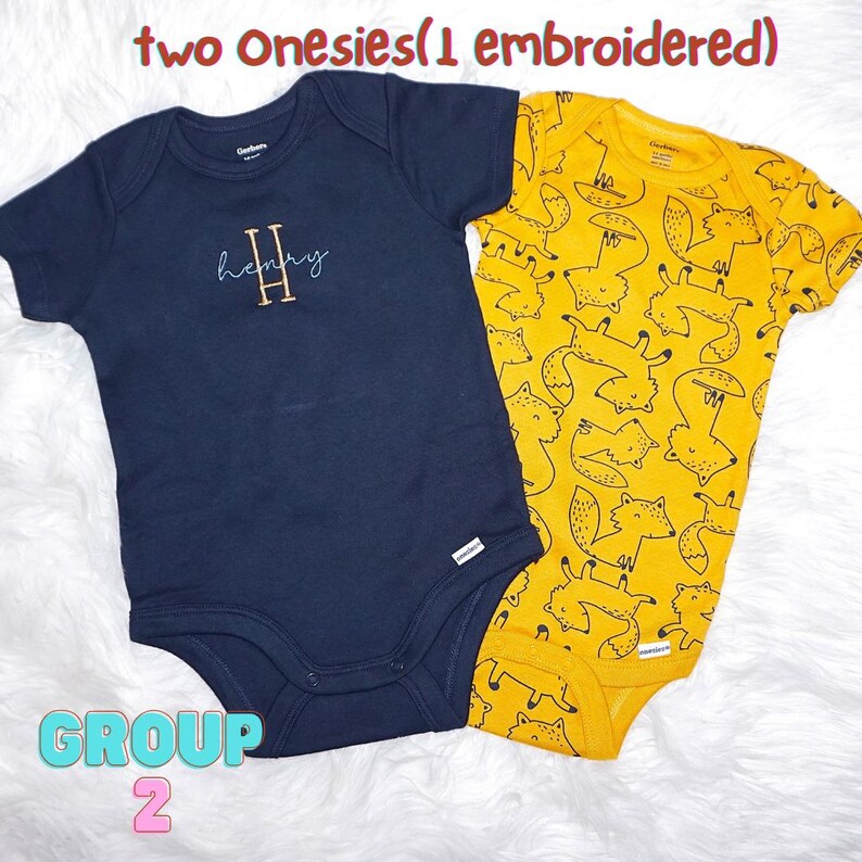 Puede incluir: Dos bodys de beb&eacute; de manga corta. Uno es azul marino liso con el nombre Henry bordado y una letra H grande. El otro es amarillo con un patr&oacute;n repetitivo de zorros en l&iacute;neas negras. El texto dice: two Onesies(1 embroidered) GROUP 2.