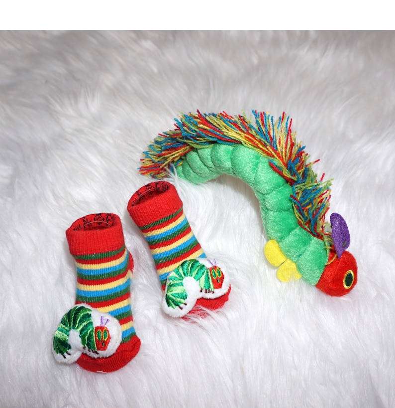 May include: Two red and yellow striped baby socks with embroidered green caterpillars. A green plush caterpillar toy with rainbow hair.
