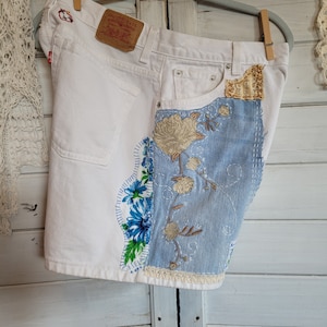 May include: White denim shorts with a patchwork design featuring blue denim, floral embroidery, and lace trim. The shorts have a Levi's brand label on the back pocket.