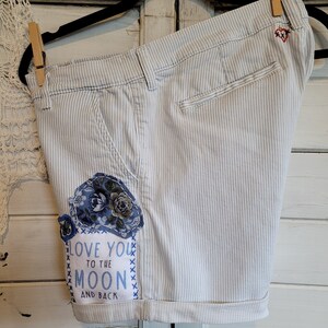 May include: White and blue striped shorts with a floral patch and a message that says "Love you to the moon and back".