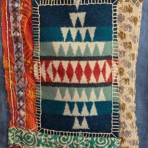 Könnte beinhalten: Ein Patchwork aus Stoffquadraten, die zu einem größeren Quadrat zusammengenäht sind. Das mittlere Quadrat zeigt ein geometrisches Muster aus weißen Dreiecken auf blauem Hintergrund. Die umliegenden Quadrate sind in verschiedenen Farben und Mustern gehalten, darunter Rot, Grün und Braun.