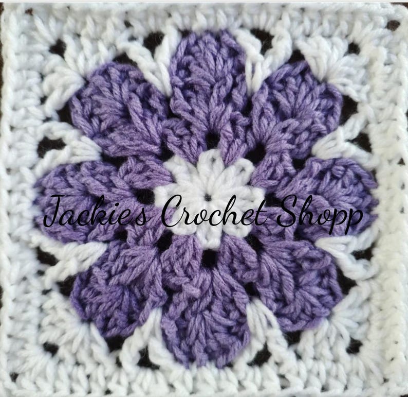 May include: A crocheted square with a purple flower in the center. The flower has five petals and is surrounded by a white border. The text "Jackie's Crochet Shop" is visible in the center of the square.