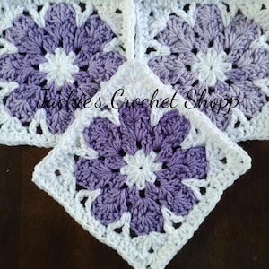 May include: Three crocheted squares with a purple and white flower design. The squares are joined together to form a larger piece. The text "Jackies Crochet Shop" is visible in the center of the image.