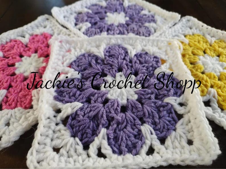 May include: Four crocheted squares with different colored flowers in the center. The squares are white with a white border. The flowers are pink, purple, yellow, and white. The text "Jackie's Crochet Shop" is visible in the center of the image.